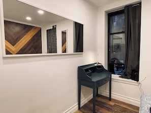 Ein Zimmer mit Spiegel, dunklem Schreibtisch, Fenster mit Vorhängen und Holzboden.