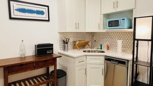 A compact kitchen with white cabinets, a microwave, a sink, and a small wooden table. - Quiet LES Designer Retro-Chic 1 Bedroom Apt Near Everything (New York)