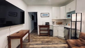 A modern kitchen with white cabinets, a wooden dining table, a sofa, and a TV mounted on the wall. - Quiet LES Designer Retro-Chic 1 Bedroom Apt Near Everything (New York)