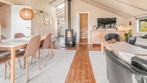 Ein geräumiger Wohnbereich mit hoher Decke, Kamin, Essbereich und Küche mit Fernseher.