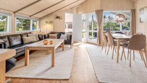 Ein geräumiger Loft mit hoher Decke, einer Essecke mit Tisch und Stühlen, einer Couch und einem großen Schiebeglasfenster, das zu einem Außenbereich führt.