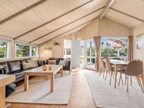 Ein geräumiger Loft mit hoher Decke, einer Essecke mit Tisch und Stühlen, einer Couch und einem großen Schiebeglasfenster, das zu einem Außenbereich führt.