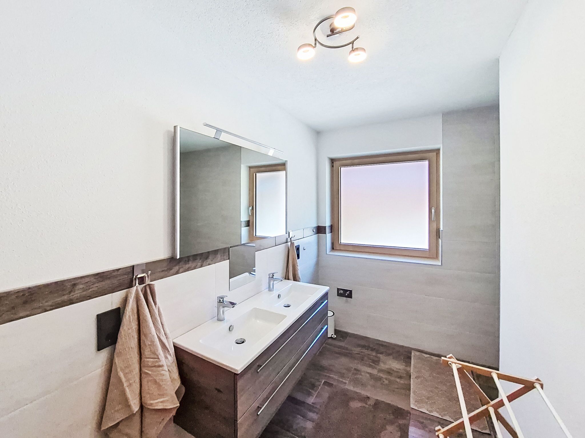 Un baño moderno con un espejo grande, dos lavamanos, un tendedero para toallas y un ventanal.