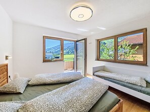 A room with two beds, a wooden headboard, a large window with a view of mountains, and a ceiling light. - Apart Wurm by Interhome (Uderns)