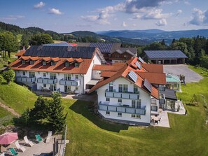 A large, multi-story building with solar panels on the roof, surrounded by lush greenery and hills in the background. - Heckenrose mit Badewelt und Sauna inkl. by Interhome (Sankt Englmar)