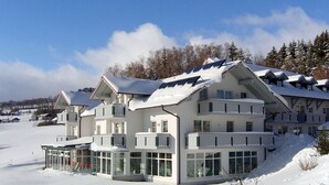 A multi-story hotel with balconies, large windows, and a snow-covered landscape. - Heckenrose mit Badewelt und Sauna inkl. by Interhome (Sankt Englmar)