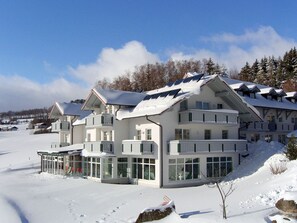 Ein mehrstöckiges Hotel mit Balkonen, großen Fenstern und einer schneebedeckten Landschaft.