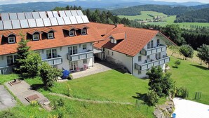 A multi-story building with a red-tiled roof, multiple balconies, and a view of the surrounding landscape. - Heckenrose mit Badewelt und Sauna inkl. by Interhome (Sankt Englmar)