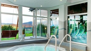 A hot tub with a view of a pool and chairs, large windows, and a tiled floor. - Heckenrose mit Badewelt und Sauna inkl. by Interhome (Sankt Englmar)