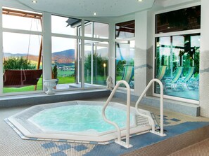 Ein Whirlpool mit Blick auf ein Schwimmbecken und Stühle, große Fenster und ein gefliester Boden.