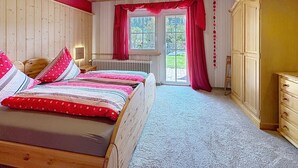 Ein Schlafzimmer mit einem hölzernen Bett, einem Heizkörper, einem Fenster mit Vorhängen und einem Kleiderschrank.