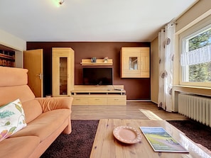 A living room with a sofa, a coffee table, a fireplace, wooden cabinets, and a window with a view. - Scherzingers Fewo by Interhome (Eisenbach)