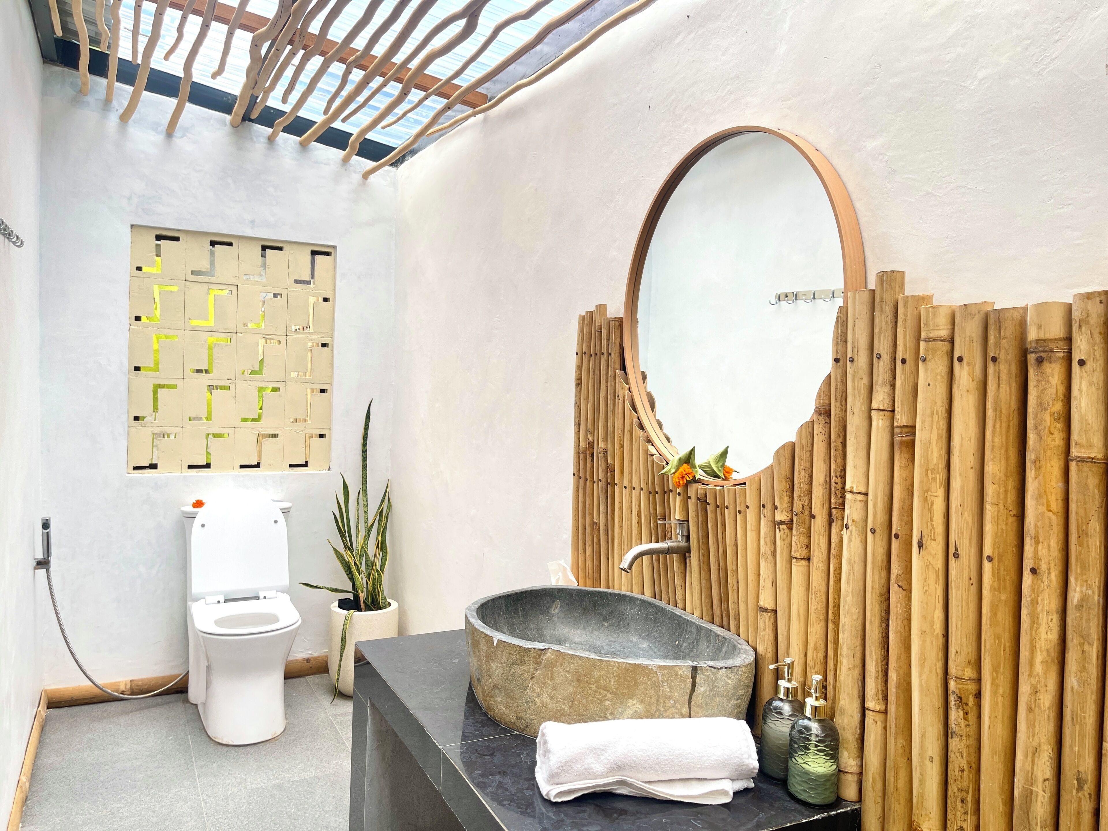 A bathroom with a toilet, a sink with a stone basin, a mirror, a potted plant, and a bamboo wall.