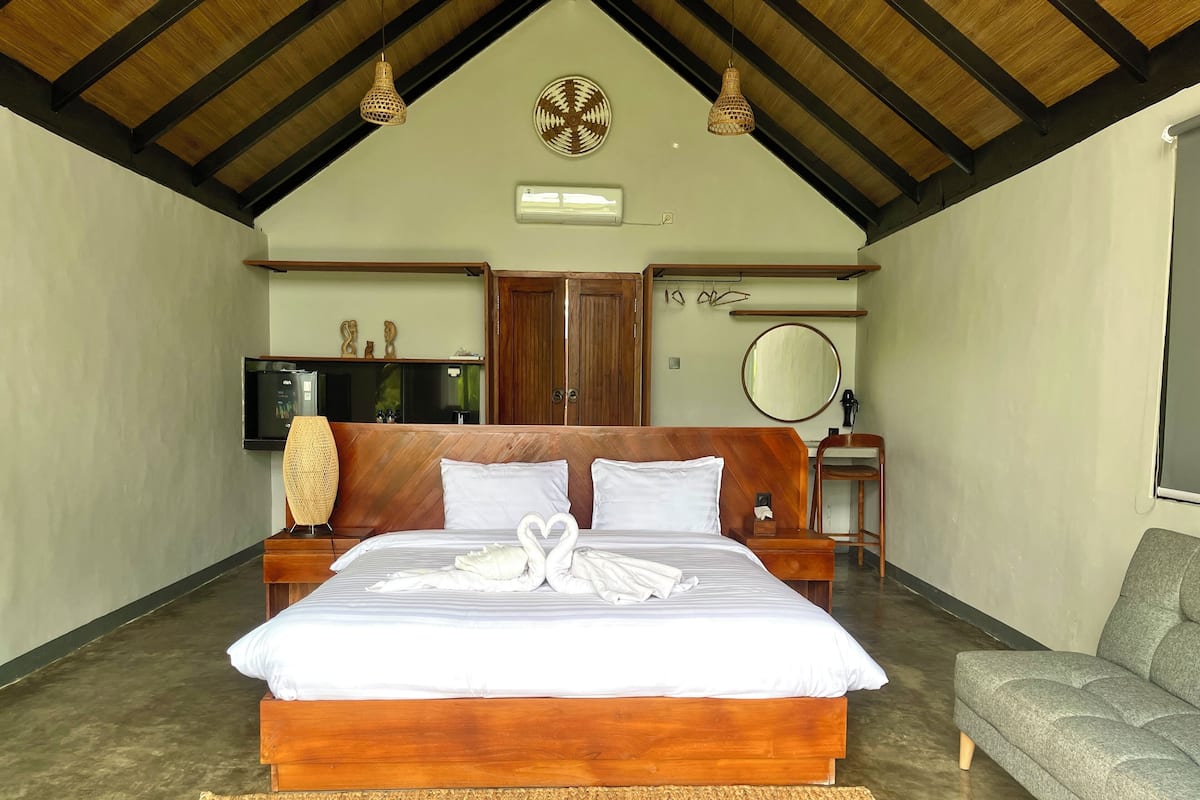 Um quarto espaçoso com uma cama grande, cabeceira de madeira e um sofá cinzento.