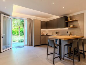 A modern kitchen with a bar area, sliding glass doors to a garden, and a minimalist design. - Apartment Renza by Interhome (Colico)