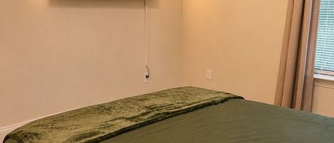 A bedroom with a bed, a wall-mounted TV displaying LSU Gators, and a window with curtains.