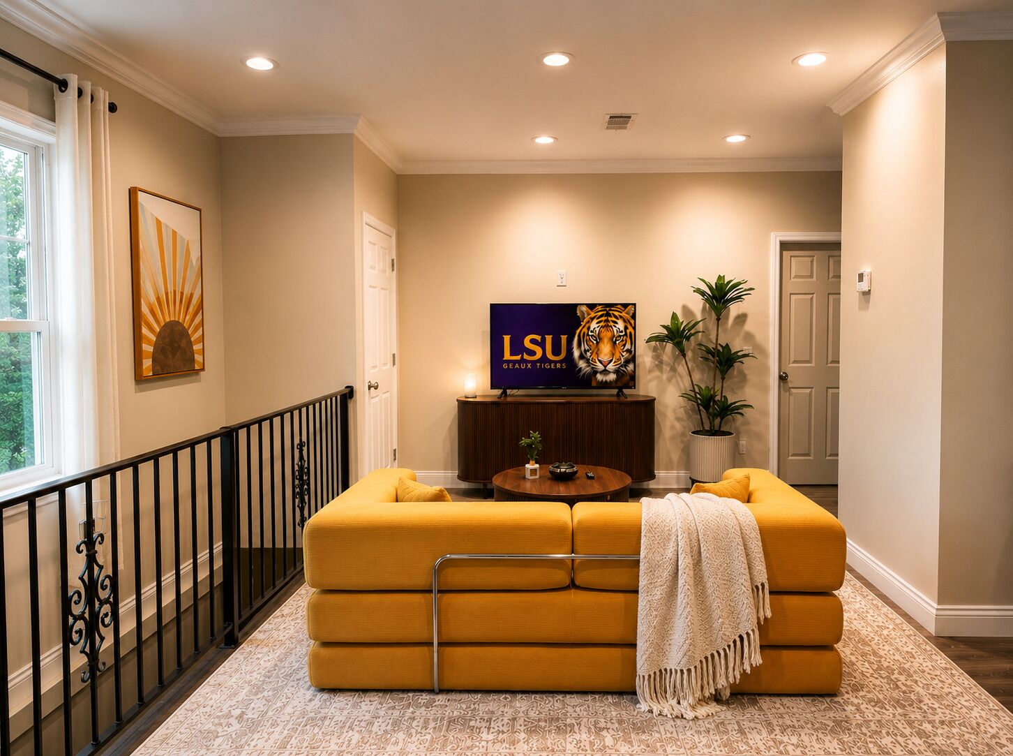 Un salon avec un canapé, une table basse, un téléviseur diffusant une émission sur l’équipe des LSU Tigers, et un escalier.