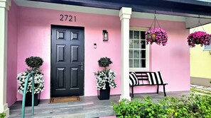 A pink building with a black door, numbered 2721, a bench, and hanging flower baskets. - Palm Beach Pink House. Walk to restaurants and shops (West Palm Beach)