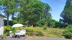 A garden with a table and chairs, a white umbrella, and a building in the background. - Coin Nature by Interhome (Montpinchon)