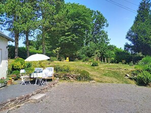 A garden with a table and chairs, a white umbrella, and a building in the background. - Coin Nature by Interhome (Montpinchon)