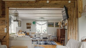 Ein gemütliches Zimmer mit Holzbalkendecke, weißen Wänden, einem Essbereich mit Tisch und Stühlen sowie einer Couch.