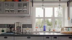 Eine Küche mit grauen Schränken, einer Kaffeemaschine, einem Wasserkocher und einem Fenster mit Blick auf Bäume.