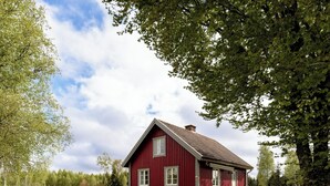 Ein rotes Holzhaus mit geneigtem Dach, einer Veranda mit Stühlen und einem Rasen.