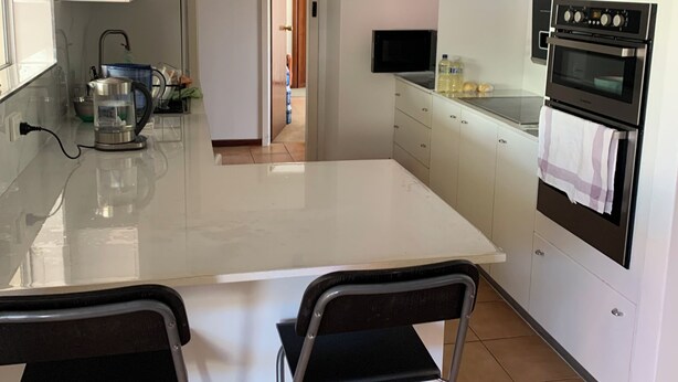 A modern kitchen with white cabinets, a stainless steel sink, a built-in oven, and a large island with two chairs. - cozy room (morley)