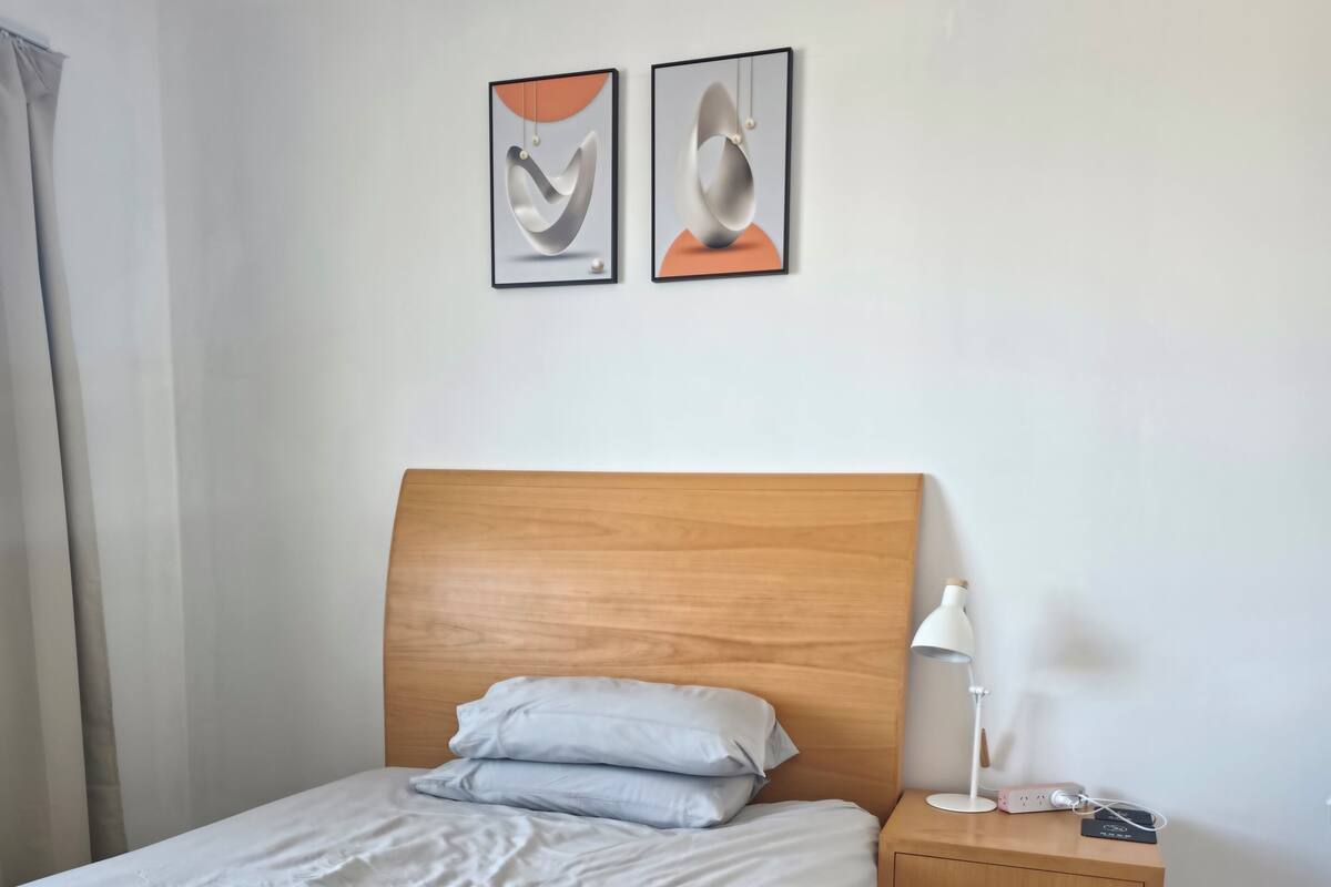 A neatly made bed with pillows, a bedside table with a lamp, and two wall art pieces.