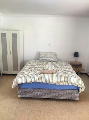 Un dormitorio con cama, armario, mesita de noche y lámpara.