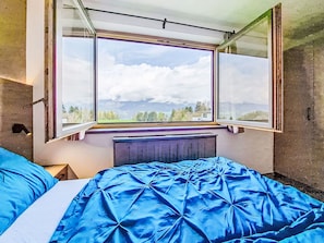 Ein Schlafzimmer mit einem großen Fenster, einer blauen Tagesdecke und einem Heizkörper.