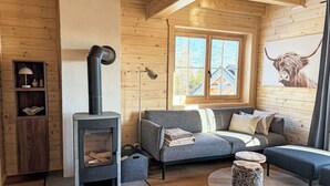 A cozy cabin interior with a fireplace, wooden walls, a sofa, and a window with a view.