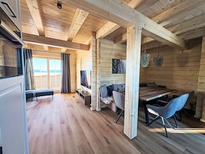 Un intérieur en bois comprenant un coin repas, un canapé, un téléviseur et une vue par une fenêtre.