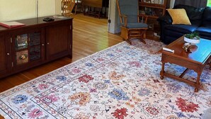 A living room with a flat-screen TV, a wooden cabinet, a sofa, a coffee table, and a patterned rug. - University House  3-bedroom with AC in charming Eugene (Eugene)