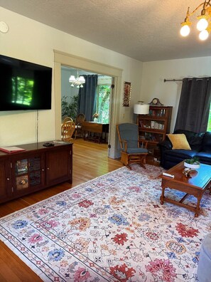 A living room with a flat-screen TV, a wooden cabinet, a sofa, a coffee table, and a patterned rug. - University House  3-bedroom with AC in charming Eugene (Eugene)