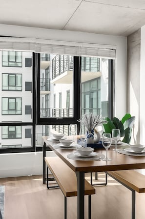 Ein moderner Essbereich mit großem Fenster, einem Holztisch und Blick auf ein Gebäude.