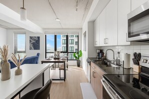 A modern kitchen with a large window, a dining area with a table set, and a view of buildings outside. - Modern 3BR Condo | Five Points South Gem S1 (Birmingham)