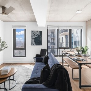 A modern living room with a sofa, a dining table, and a large window. - Modern 3BR Condo | Five Points South Gem S1 (Birmingham)