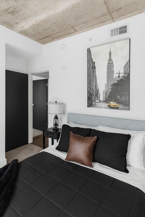 Ein Schlafzimmer mit Bett, Nachttisch, Lampe, Tür und einem Stadtbild an der Wand.
