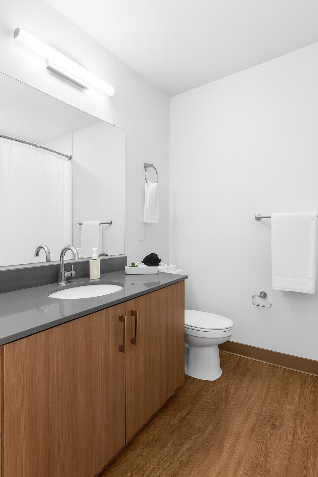 A modern bathroom with a wooden vanity, a white sink, a mirror, a toilet, and a towel rack.