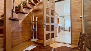 Eine Holztreppe führt zu einem Raum mit Glastür, Kleiderhaken und einem Ventilator.