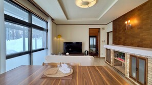 Ein modernes Wohnzimmer mit Fernseher, Sofa, Esstisch aus Holz und Kamin.