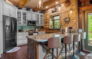 A kitchen with wooden walls, a stainless steel refrigerator, a microwave, and a large island with bar stools. - The Missing Peace Cabin - Hot Tub, Private 3BR Mountain Reset Near Pisgah Nat’l (Brevard)