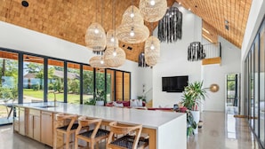 A spacious kitchen with a large island, wooden chairs, and hanging light fixtures. - Dazzling Design Meets Spectacular Views (Eatonton)