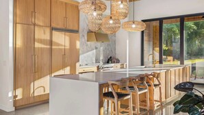 A modern kitchen with wooden cabinets, a marble countertop, and a large island with bar stools. - Dazzling Design Meets Spectacular Views (Eatonton)