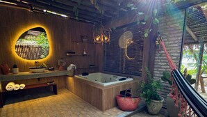 A bathroom with a bathtub, a sink, and a mirror. There are plants and a hammock. - Hotel Boutique Quinta Três Marias (Paracuru)