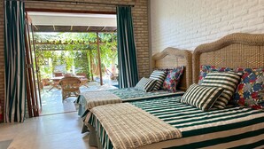 A room with two beds, a wicker headboard, striped bedding, and a view of an outdoor area with chairs and greenery. - Hotel Boutique Quinta Três Marias (Paracuru)