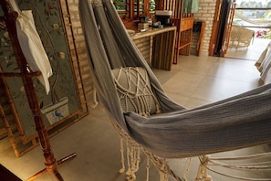 Una silla hamaca en una habitación con pared de ladrillo, una mesa de madera y vistas a la vegetación.