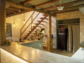 Una cocina con una escalera de madera, un refrigerador y focos colgantes.