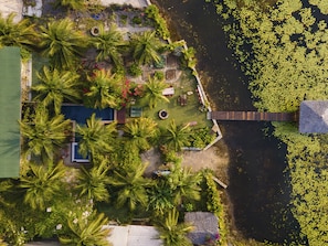 Vista aérea de una propiedad con piscina, palmeras y un muelle que se adentra en el agua.